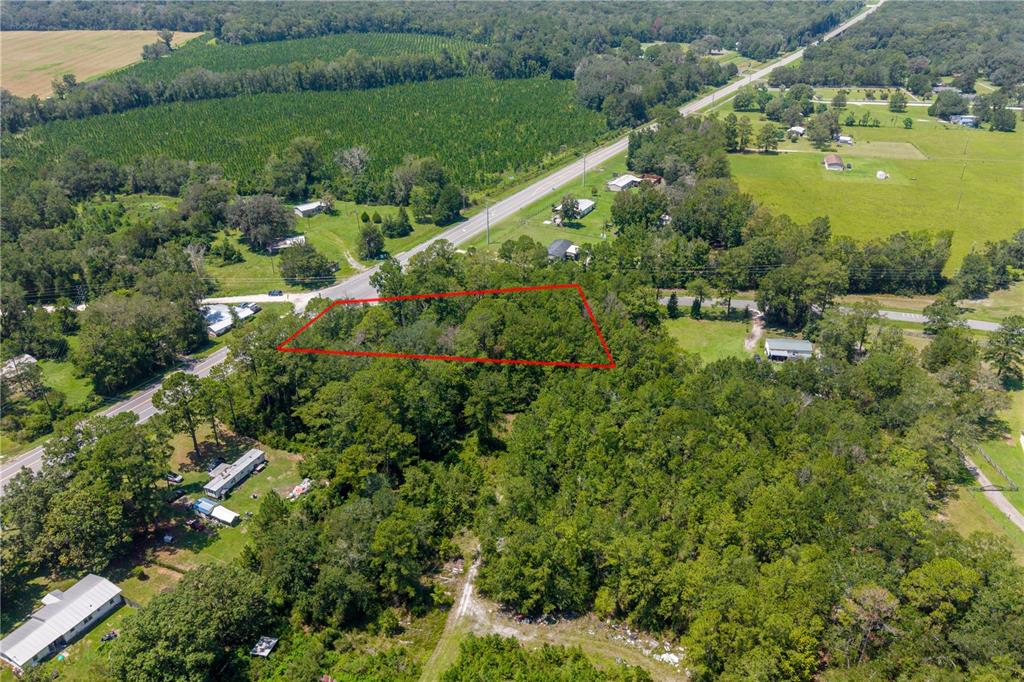 An aerial view shows a wooded lot outlined in red near a road and fields — TBD SR 100, LAKE BUTLER, FL