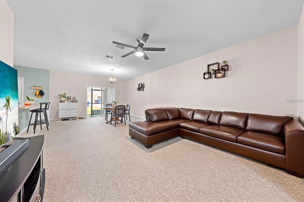 A living room features a brown leather sectional, beige carpeting, and an adjacent dining area — 1619 REFLECTION COVE, ST CLOUD, FL