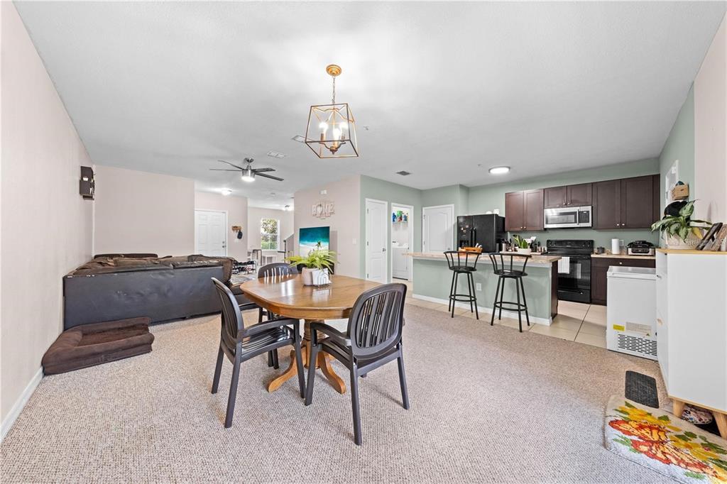 An open-concept living and dining area features carpeted floors, a kitchen island, and dark cabinetry — 1619 REFLECTION COVE, ST CLOUD, FL