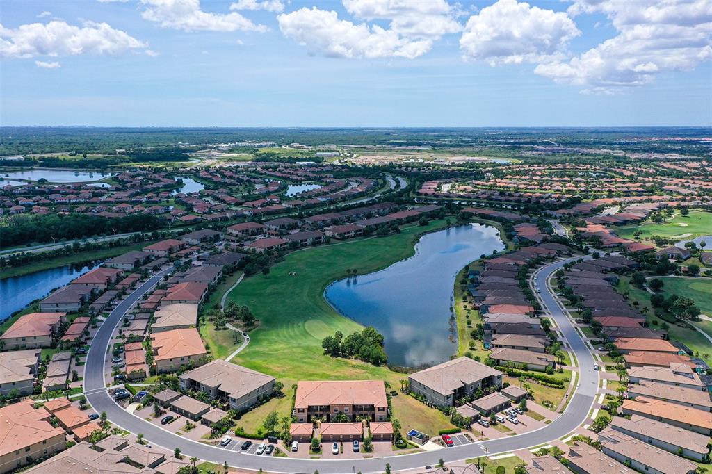 An aerial view of a suburban residential community featuring houses surrounding a central lake — 13823 MESSINA LOOP UNIT 202, BRADENTON, FL