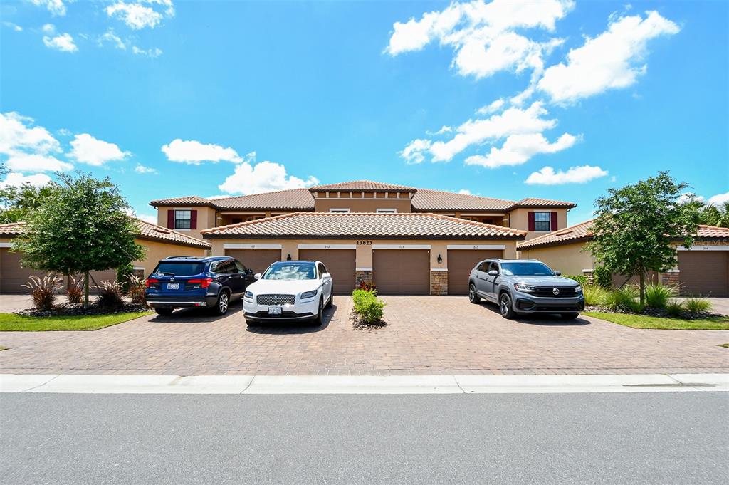 A multi-unit residential building with a tiled roof, garage doors, and three parked cars — 13823 MESSINA LOOP UNIT 202, BRADENTON, FL