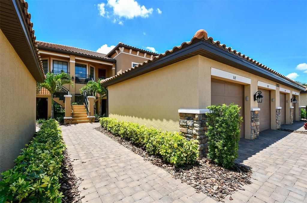 A paved walkway leads to a tan building with multiple garage doors and exterior stairs — 13823 MESSINA LOOP UNIT 202, BRADENTON, FL