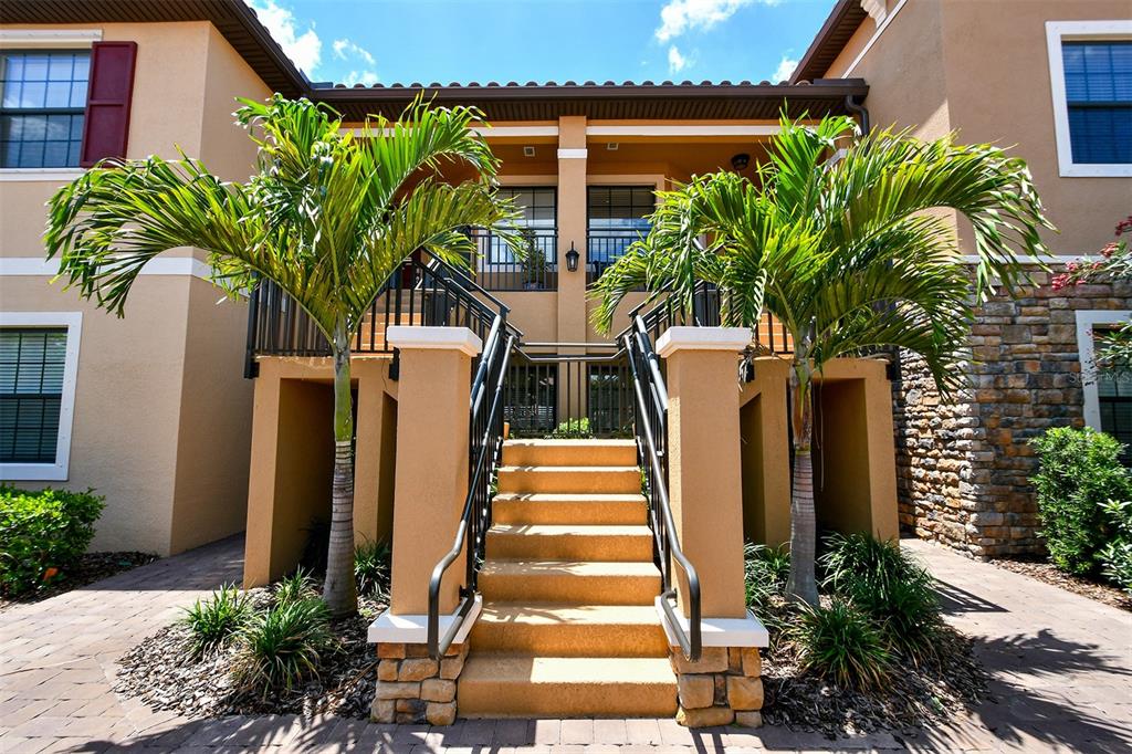 Exterior view of a multi-story apartment building with a central staircase and two palm trees — 13823 MESSINA LOOP UNIT 202, BRADENTON, FL