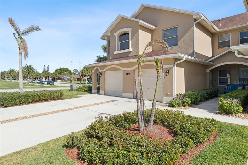 A two-story tan townhouse with a two-car garage and a small palm tree garden — 907 OCASO LANE UNIT 101, ROCKLEDGE, FL