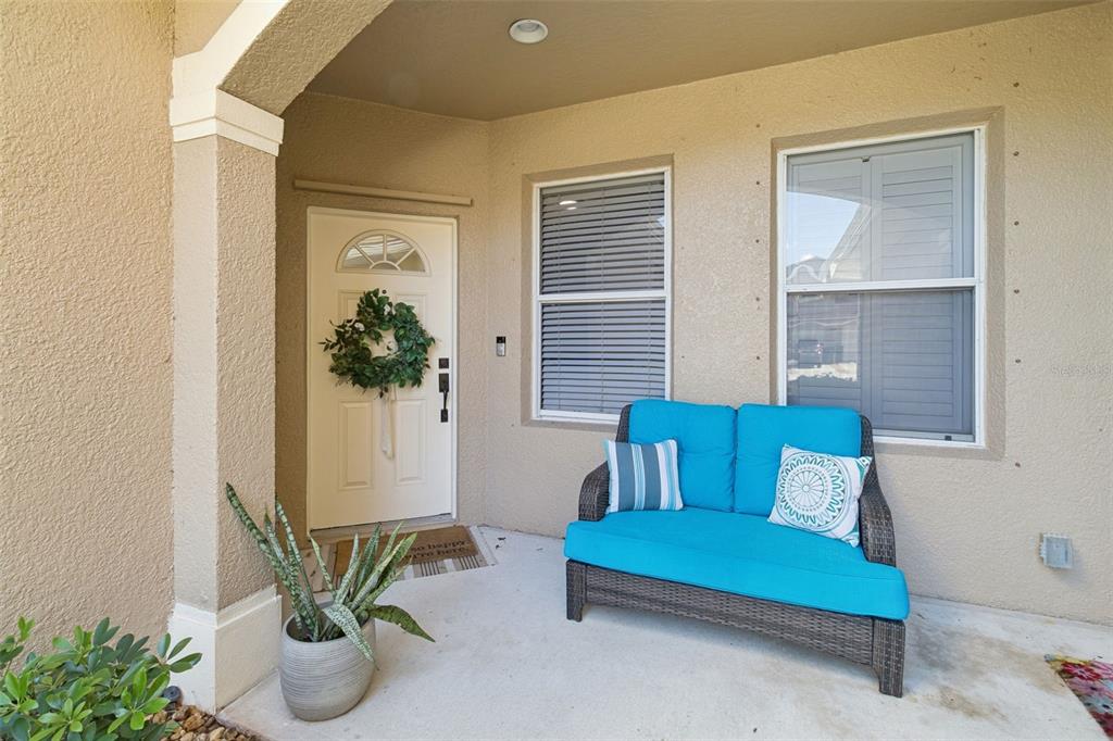 A covered front porch features a white door with a wreath and a blue loveseat — 907 OCASO LANE UNIT 101, ROCKLEDGE, FL