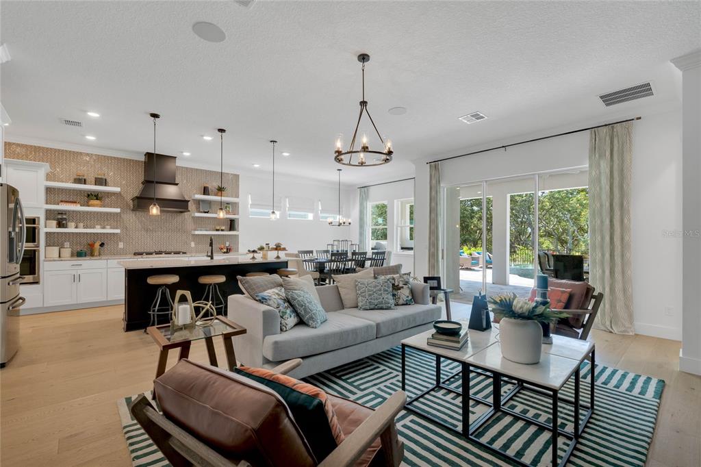 An open-concept kitchen and living area features a large island, modern lighting, and sliding glass doors — 17418 HONEYBELL TANGELO COURT, WINTER GARDEN, FL
