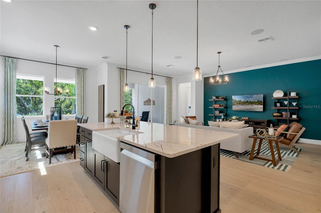 A modern open-concept kitchen features a large quartz island, dark cabinetry, and a teal accent wall — 17418 HONEYBELL TANGELO COURT, WINTER GARDEN, FL