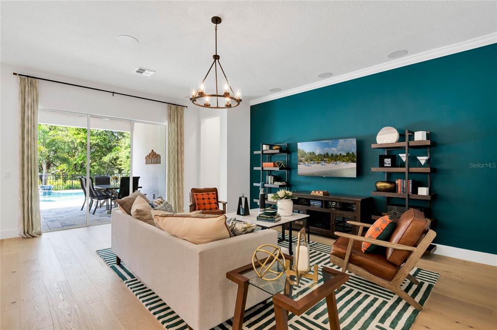 A living room features a teal accent wall, a television, shelving, and a sliding glass door — 17418 HONEYBELL TANGELO COURT, WINTER GARDEN, FL
