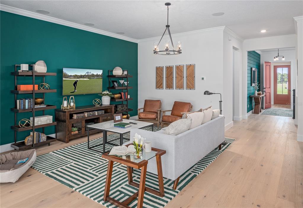 A living room features a teal accent wall, a light gray sofa, and wood flooring — 17418 HONEYBELL TANGELO COURT, WINTER GARDEN, FL
