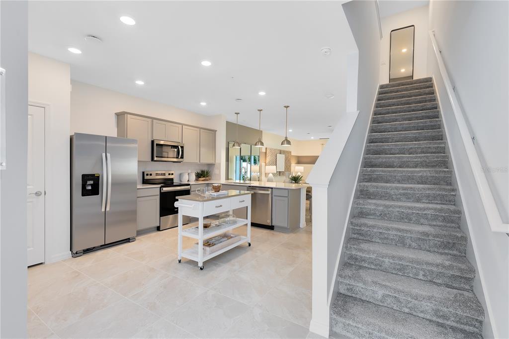 A kitchen with stainless steel appliances and a center island sits beside a carpeted staircase — 5005 SUNRISE ESTATE DRIVE, WEST MELBOURNE, FL