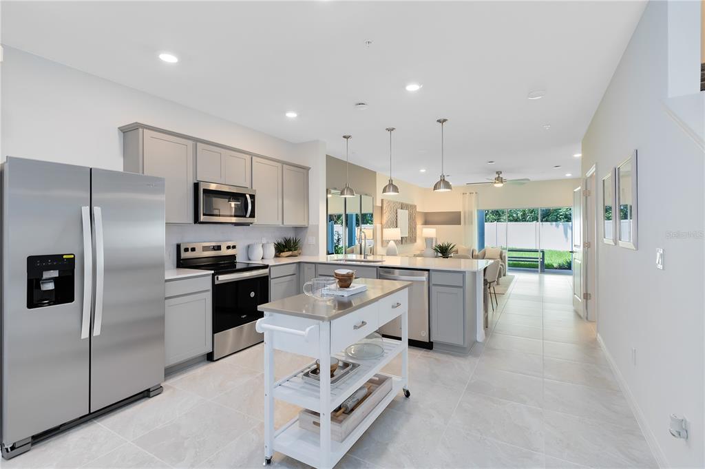 A modern kitchen features gray cabinets, stainless steel appliances, a white rolling island, and tile flooring — 5005 SUNRISE ESTATE DRIVE, WEST MELBOURNE, FL