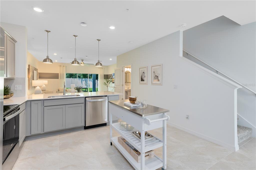 A modern kitchen features gray cabinets, stainless steel appliances, a rolling island, and a staircase — 5005 SUNRISE ESTATE DRIVE, WEST MELBOURNE, FL