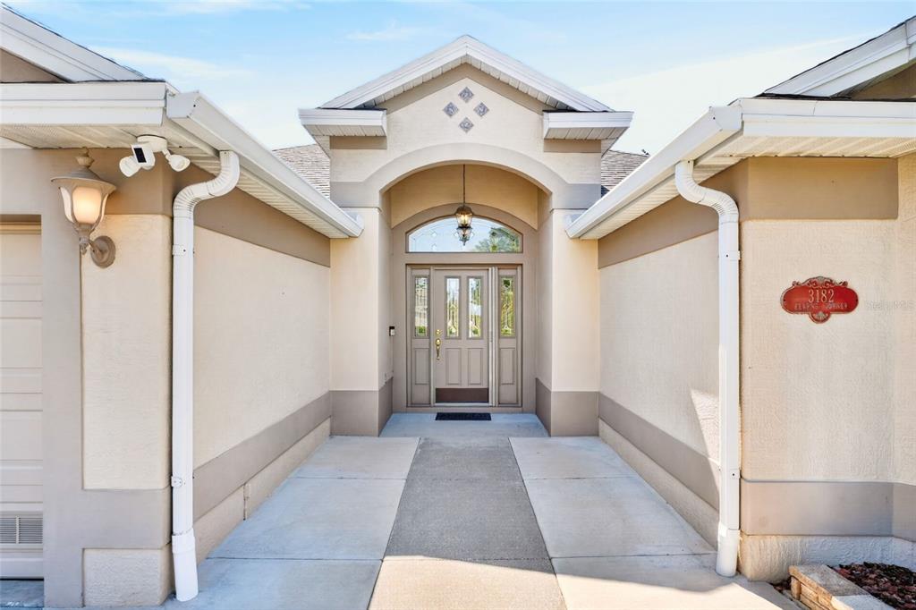 The exterior view shows a beige house entrance with a front door and concrete walkway — 3182 KEARNS CORNER, THE VILLAGES, FL