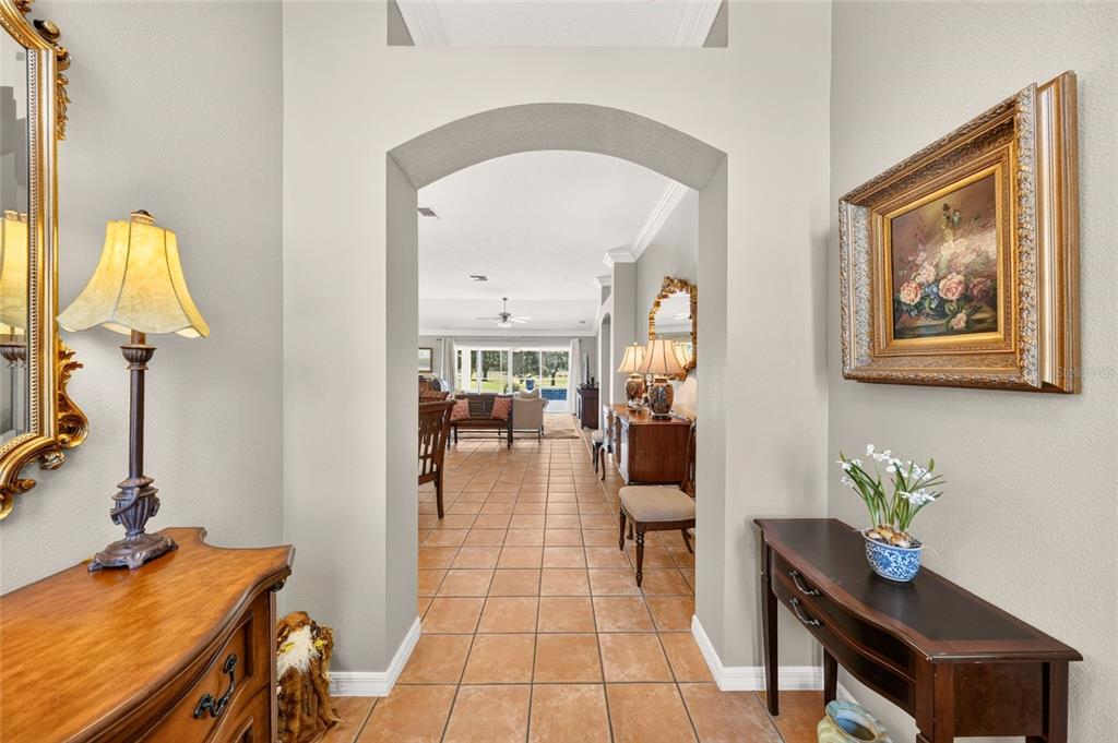 A tiled entryway leads through an arched doorway into a living area with a view outside — 3182 KEARNS CORNER, THE VILLAGES, FL