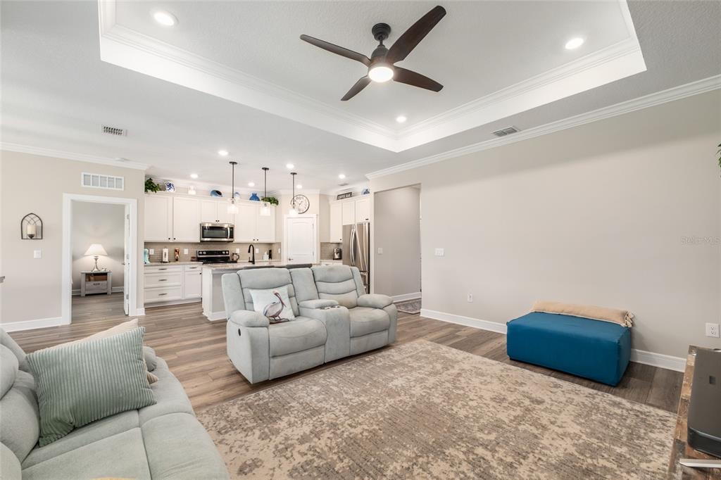 A living room with a tray ceiling, ceiling fan, and open access to a kitchen — 9407 SW 52ND LOOP, OCALA, FL