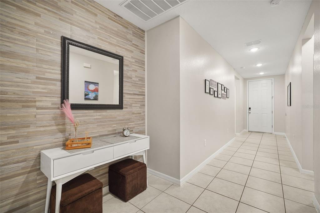 A hallway features a white console table, two brown ottomans, and a wood-paneled accent wall — 428 MCKENNA DRIVE, WINTER HAVEN, FL