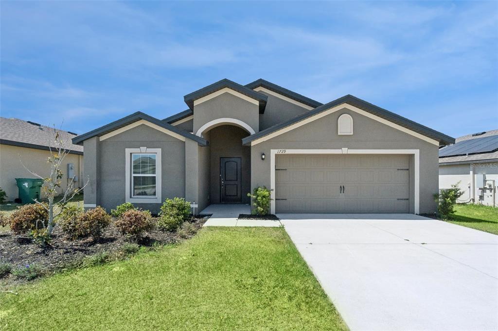 A single-story house with a gray stucco exterior, a two-car garage, and a front lawn — 1729 CANAAN LOOP, DUNDEE, FL