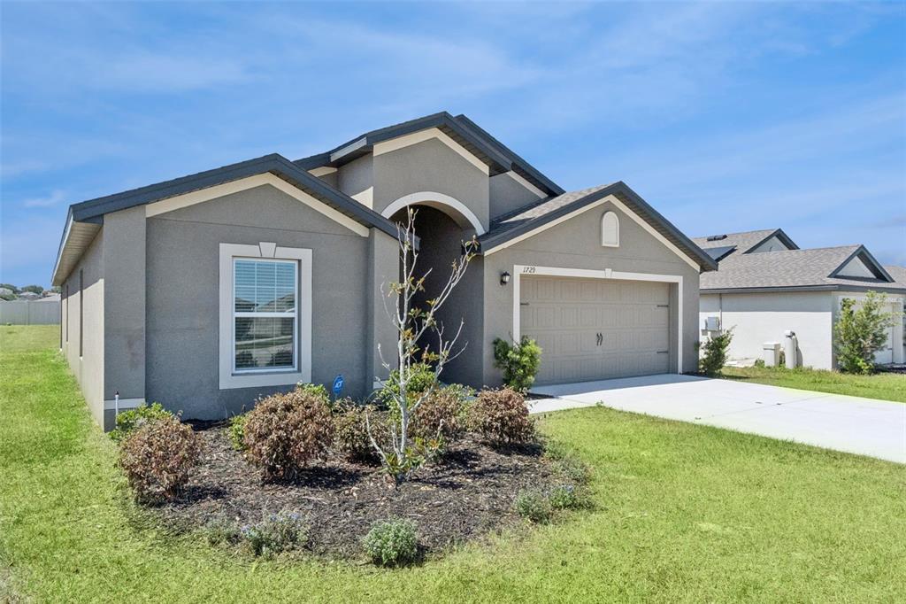 A single-story suburban house with a gray stucco exterior, a two-car garage, and landscaping — 1729 CANAAN LOOP, DUNDEE, FL
