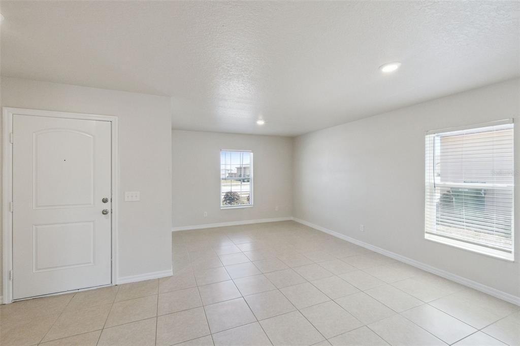 An empty room with light-colored tile flooring, white walls, a front door, and two windows — 1729 CANAAN LOOP, DUNDEE, FL