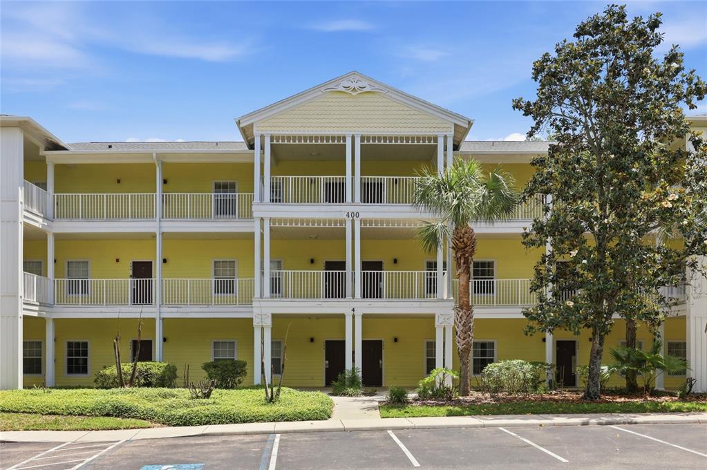 A three-story yellow apartment building with white railings and a palm tree in front — 410 LUCAYA LOOP UNIT 4204, DAVENPORT, FL
