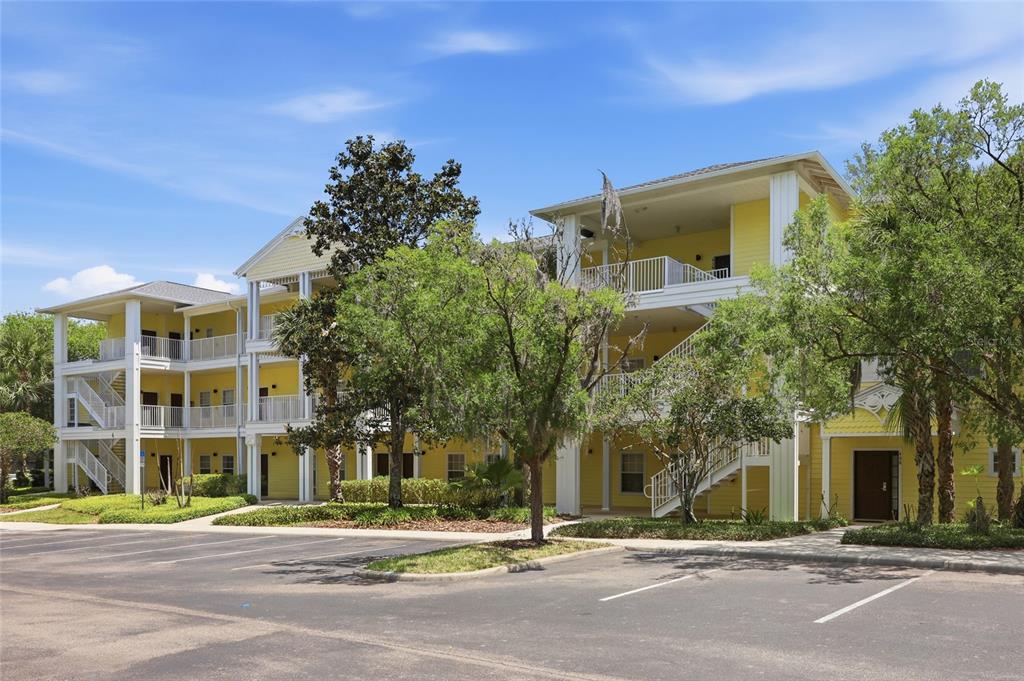 A three-story yellow apartment building with exterior staircases and a parking lot in front — 410 LUCAYA LOOP UNIT 4204, DAVENPORT, FL