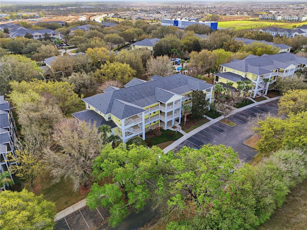 An aerial view shows a yellow multi-story apartment building surrounded by trees and parking lots — 410 LUCAYA LOOP UNIT 4204, DAVENPORT, FL