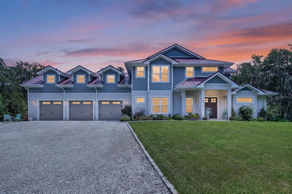 A two-story blue house with a three-car garage and a gravel driveway at sunset — 8 LEXINGTON COURT, FLAGLER BEACH, FL