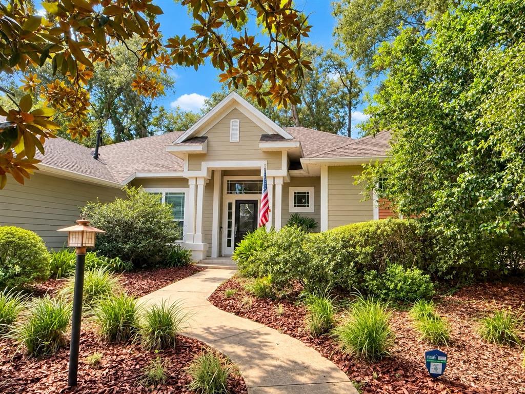 A tan house with a front walkway, landscaping, and an American flag by the door — 8718 SW 8TH PLACE, GAINESVILLE, FL