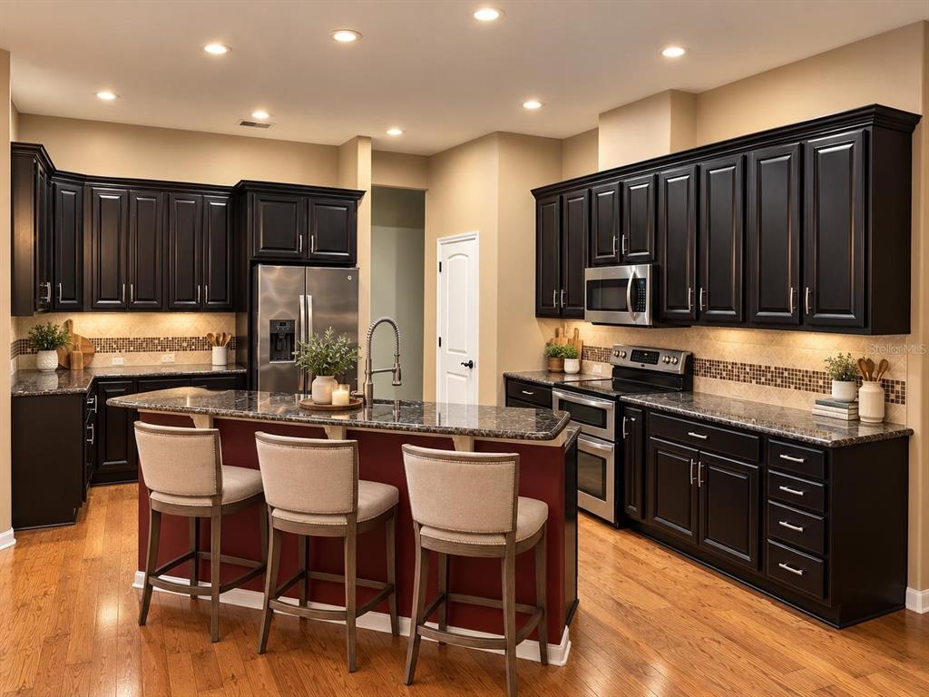 A kitchen features dark wood cabinets, a granite-topped island with three chairs, and hardwood floors — 8718 SW 8TH PLACE, GAINESVILLE, FL