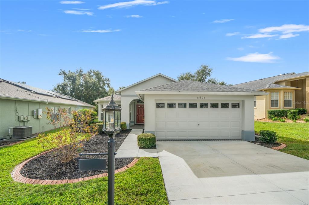 A single-story house with a two-car garage, a red front door, and a landscaped yard — 18208 BRELAND DRIVE, HUDSON, FL
