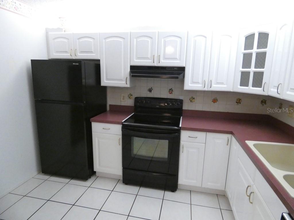 A kitchen features white cabinets, black appliances, burgundy countertops, and white tiled flooring — 104 BOUGH AVENUE UNIT 104, CLEARWATER, FL
