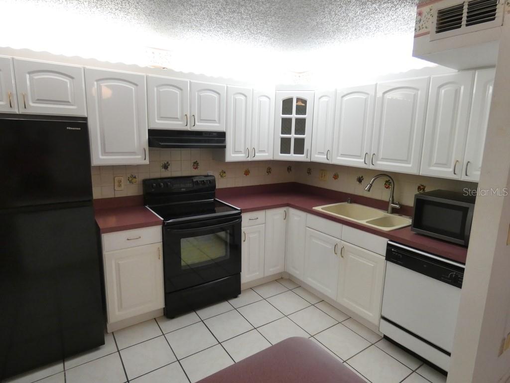 A kitchen with white cabinets, burgundy countertops, black appliances, and white tiled flooring — 104 BOUGH AVENUE UNIT 104, CLEARWATER, FL