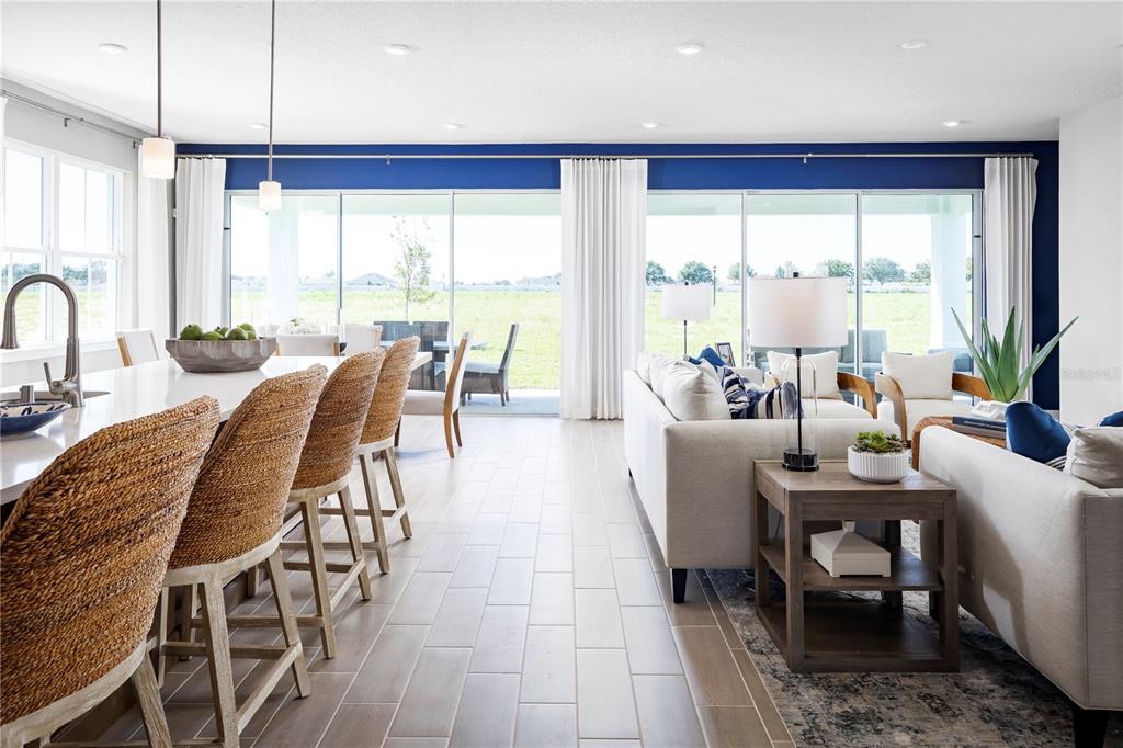 An open-concept living room and kitchen featuring a blue accent wall and sliding glass doors — 22177 PINE GROVE LOOP, LEESBURG, FL