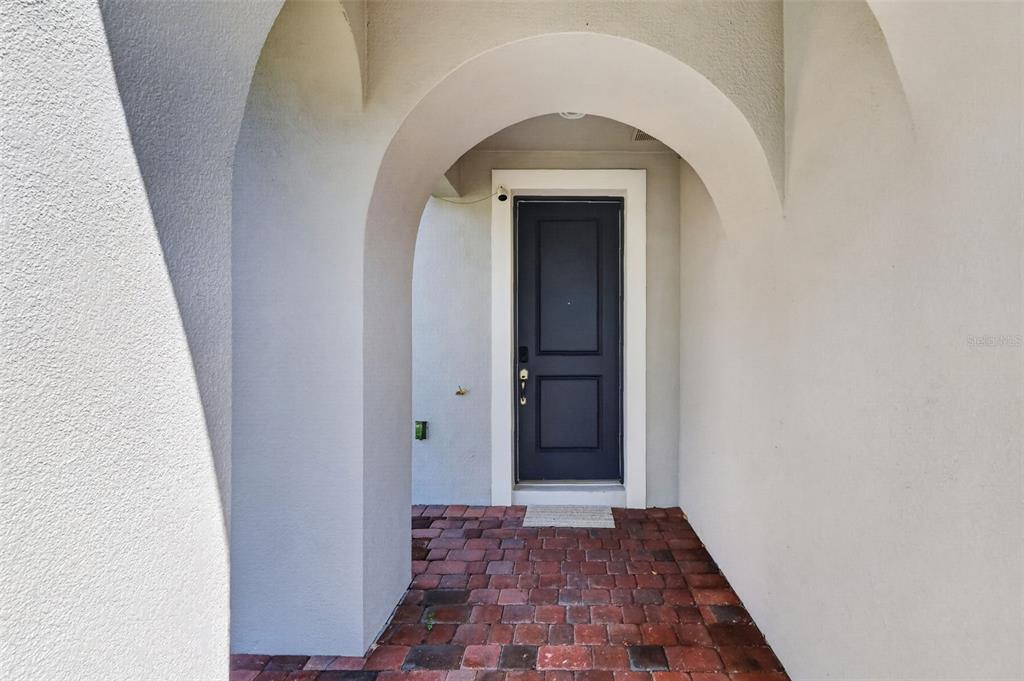 A dark front door is recessed within a stucco archway over a brick-paved entryway — 1090 HARBOR RIDGE DRIVE, POINCIANA, FL