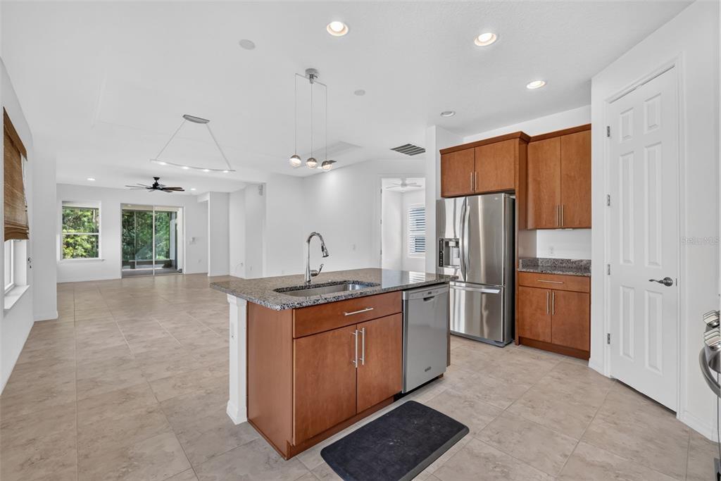 A kitchen with wood cabinets, granite countertops, and a center island overlooks an open living area — 1090 HARBOR RIDGE DRIVE, POINCIANA, FL