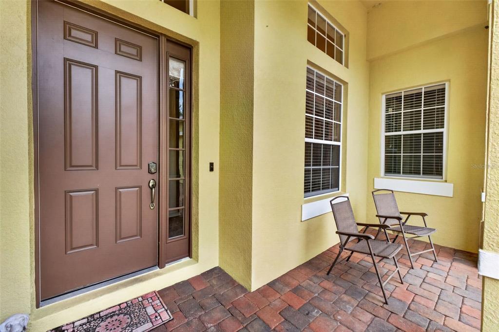 A brown front door and two chairs sit on a paved porch with yellow walls — 2623 PALASTRO WAY, OCOEE, FL