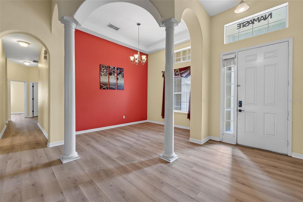 An entryway features light wood flooring, white columns, and a bright red accent wall — 2623 PALASTRO WAY, OCOEE, FL