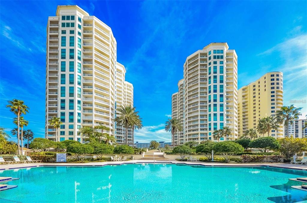A swimming pool sits in front of three tall, multi-story residential apartment buildings — 1180 GULF BOULEVARD UNIT 906, CLEARWATER BEACH, FL