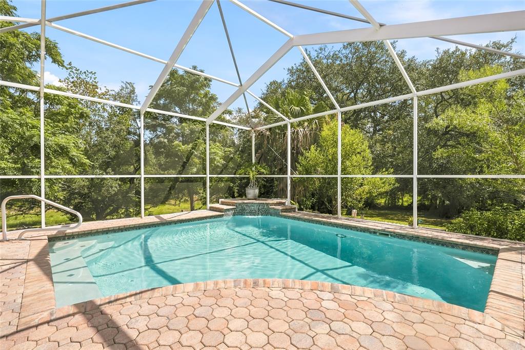 A screened-in swimming pool with a small waterfall feature and a brick paver deck — 8206 NIGHTINGALE ROAD, WEEKI WACHEE, FL