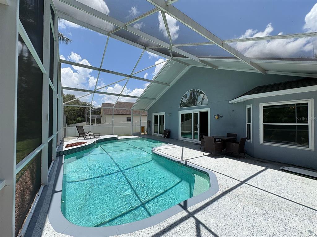 A screened-in swimming pool sits on a patio next to a light blue house — 2791 PICADILLY CIRCLE, KISSIMMEE, FL