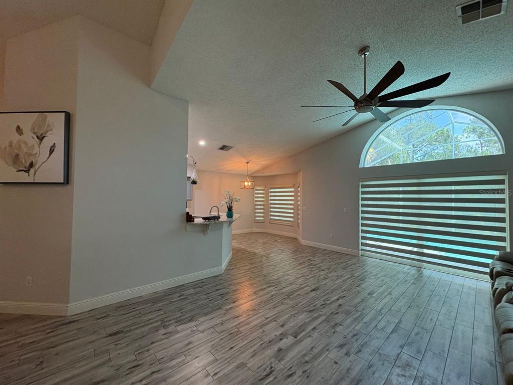 A living room with wood-look tile flooring, a vaulted ceiling, and a large arched window — 2791 PICADILLY CIRCLE, KISSIMMEE, FL