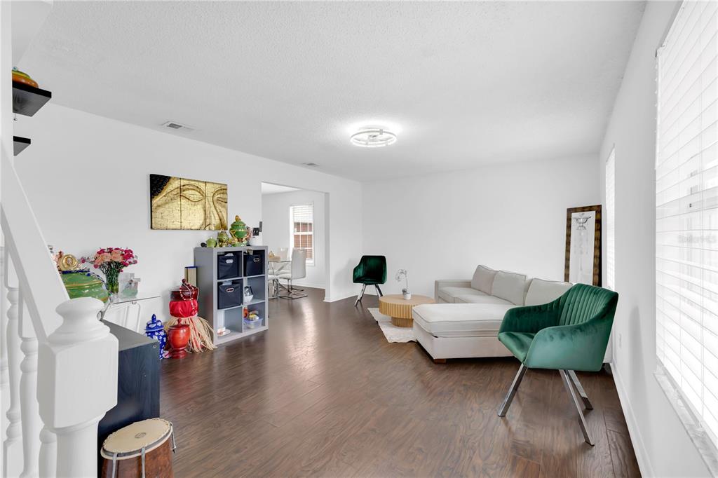 A living room with dark wood flooring, a white sectional sofa, and green velvet chairs — 5054 ARRAPAHOE STREET, ST CLOUD, FL
