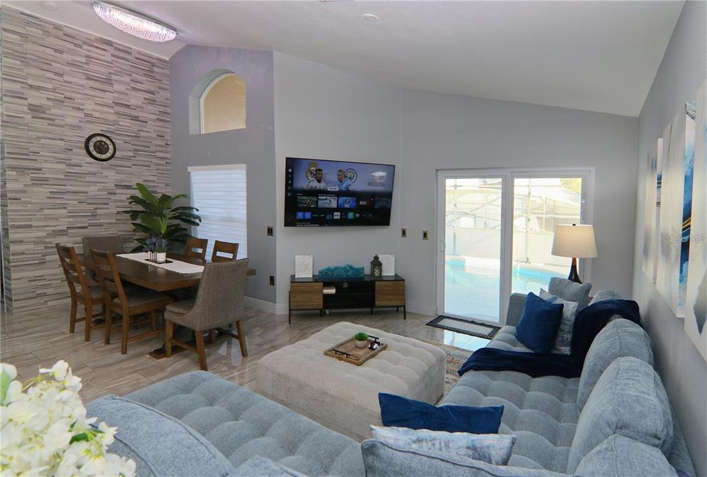 A living and dining area features a stone accent wall, light blue sofa, and pool view — 1470 WEDGE WAY, HAINES CITY, FL