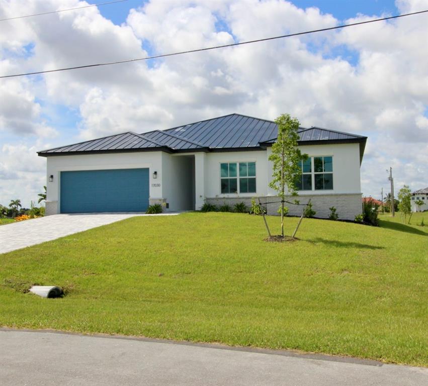 A single-story house with a blue garage door, white stucco walls, and a metal roof — 17030 ESPANA CIRCLE, PUNTA GORDA, FL