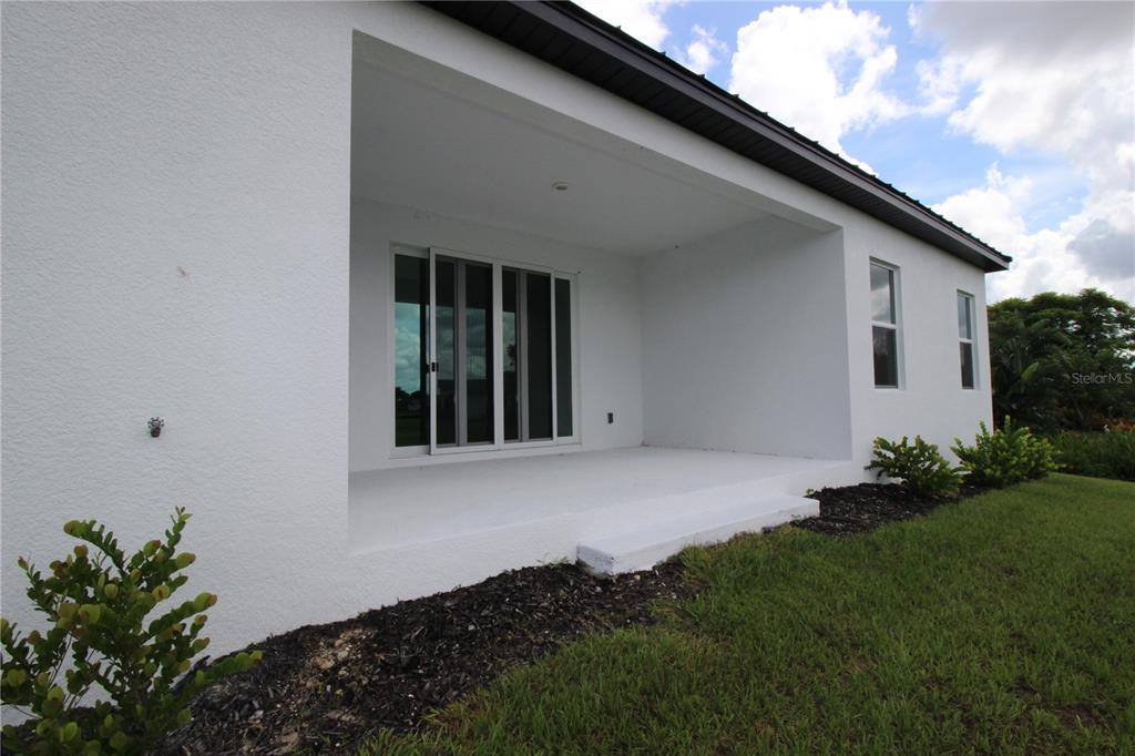 A white exterior house features a covered concrete patio with sliding glass doors — 17030 ESPANA CIRCLE, PUNTA GORDA, FL