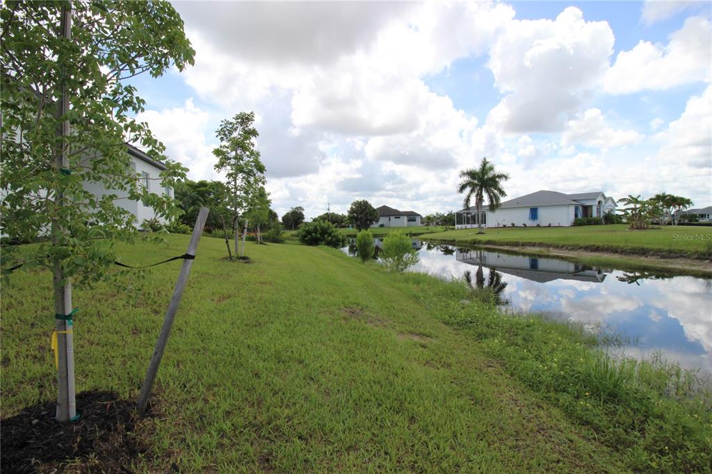 A grassy yard slopes down to a canal behind several houses under a cloudy sky — 17030 ESPANA CIRCLE, PUNTA GORDA, FL