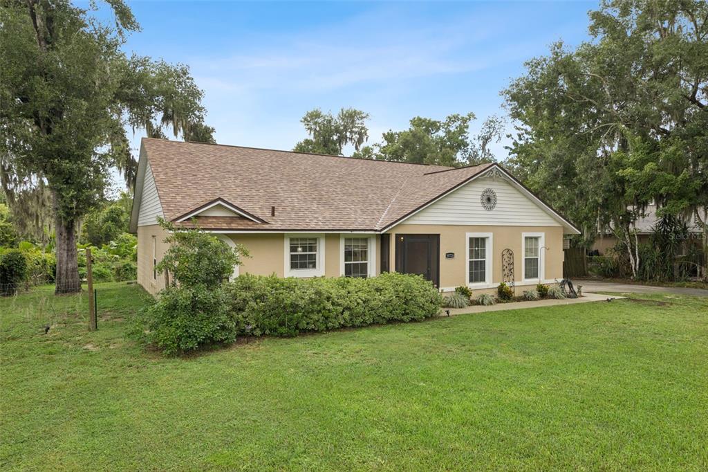 A single-story house with a tan stucco exterior, brown shingle roof, and a front hedge — 30724 FAIRVIEW AVENUE, TAVARES, FL