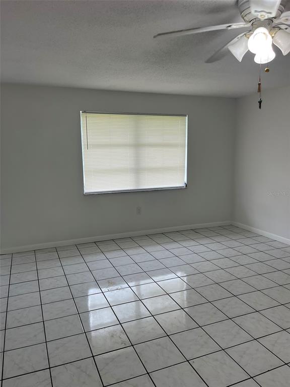 An empty room features white walls, a ceiling fan, and white tiled flooring — 8956 SE 65TH WAY, OKEECHOBEE, FL