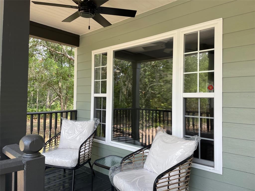 A covered porch features two chairs with plastic-covered cushions and a large multi-pane window — 7152 SANDY LANE, WESLEY CHAPEL, FL