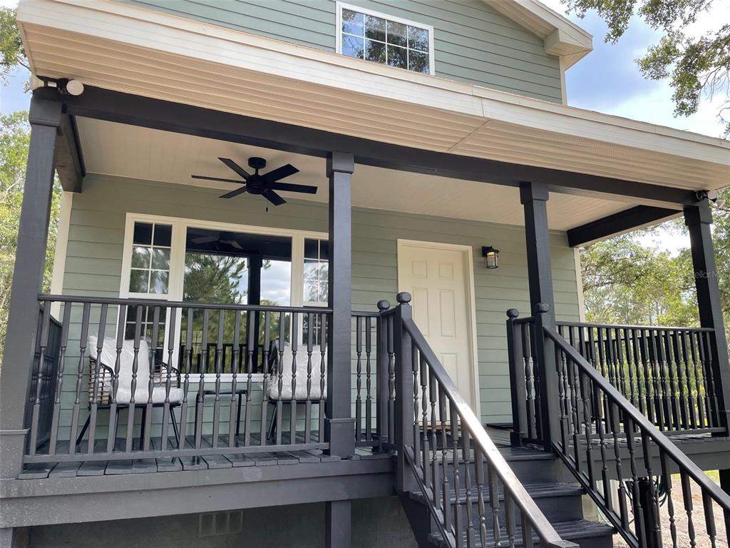 A green house exterior features a covered porch with black railings, stairs, and a ceiling fan — 7152 SANDY LANE, WESLEY CHAPEL, FL
